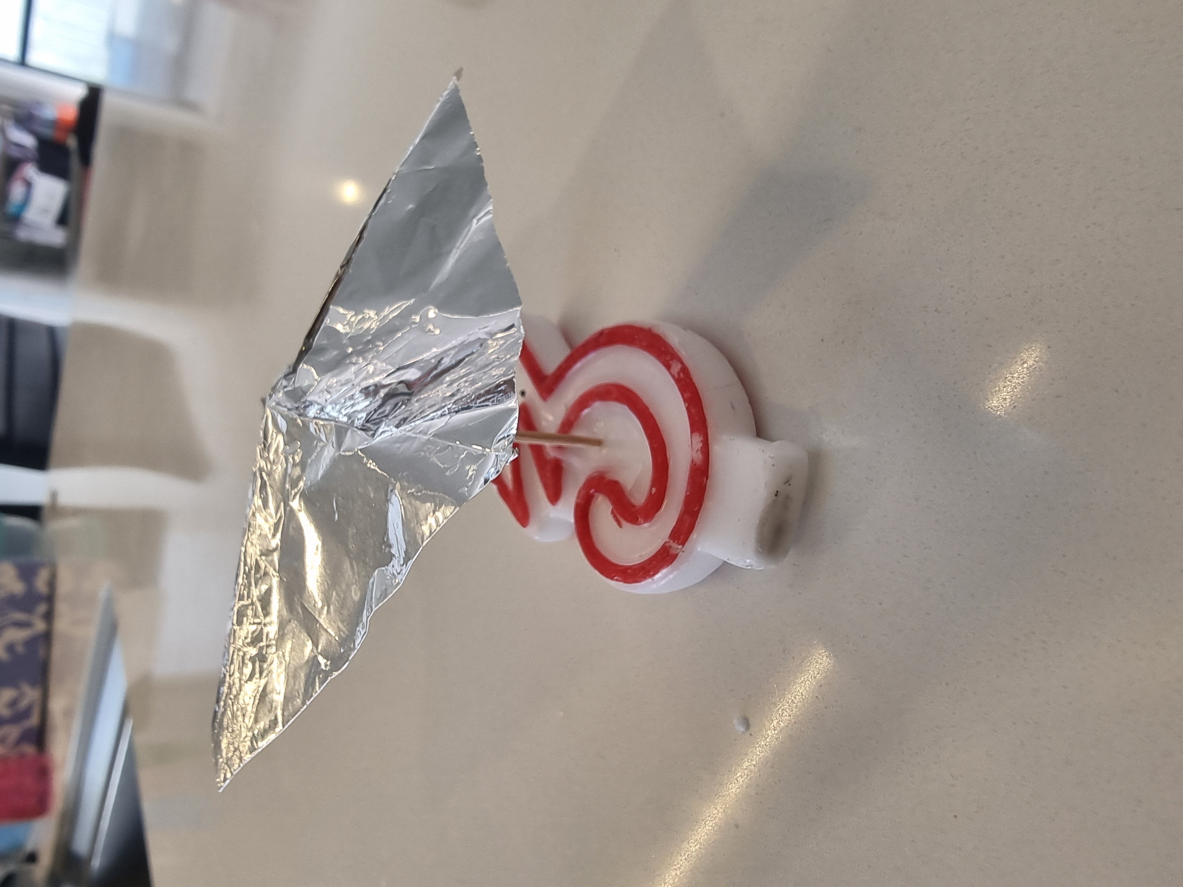 psi wheel made from a square piece of tinfoil balanced on a toothpick that is stuck on a 3 candle